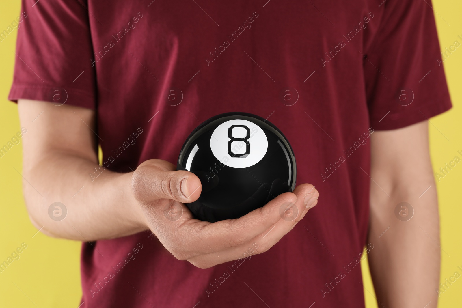 Photo of Man holding magic eight ball on yellow background, closeup