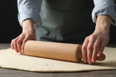 Photo of Woman rolling raw dough at wooden table, closeup