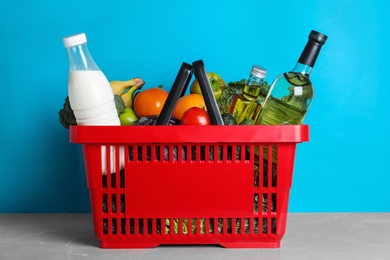 Photo of Shopping basket with grocery products on grey table against light blue background