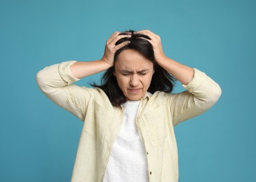 Photo of Mature woman suffering from headache on light blue background