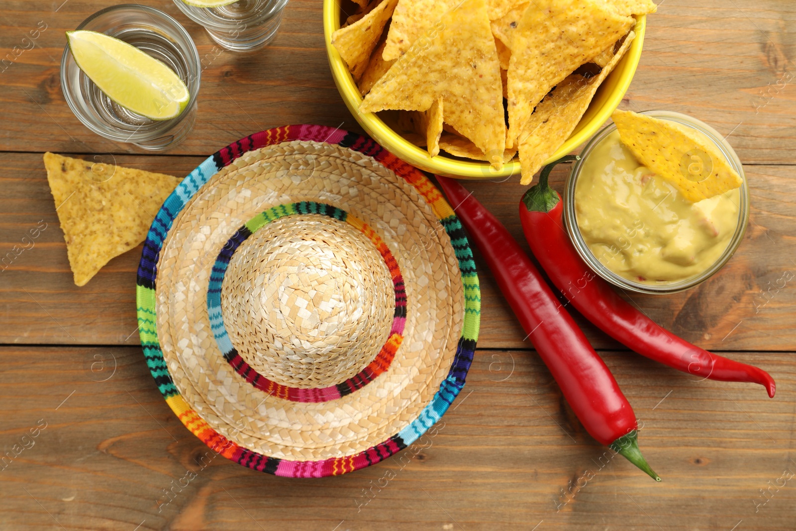 Photo of Mexican sombrero hat, tequila, chili peppers, nachos chips and guacamole on wooden table, flat lay
