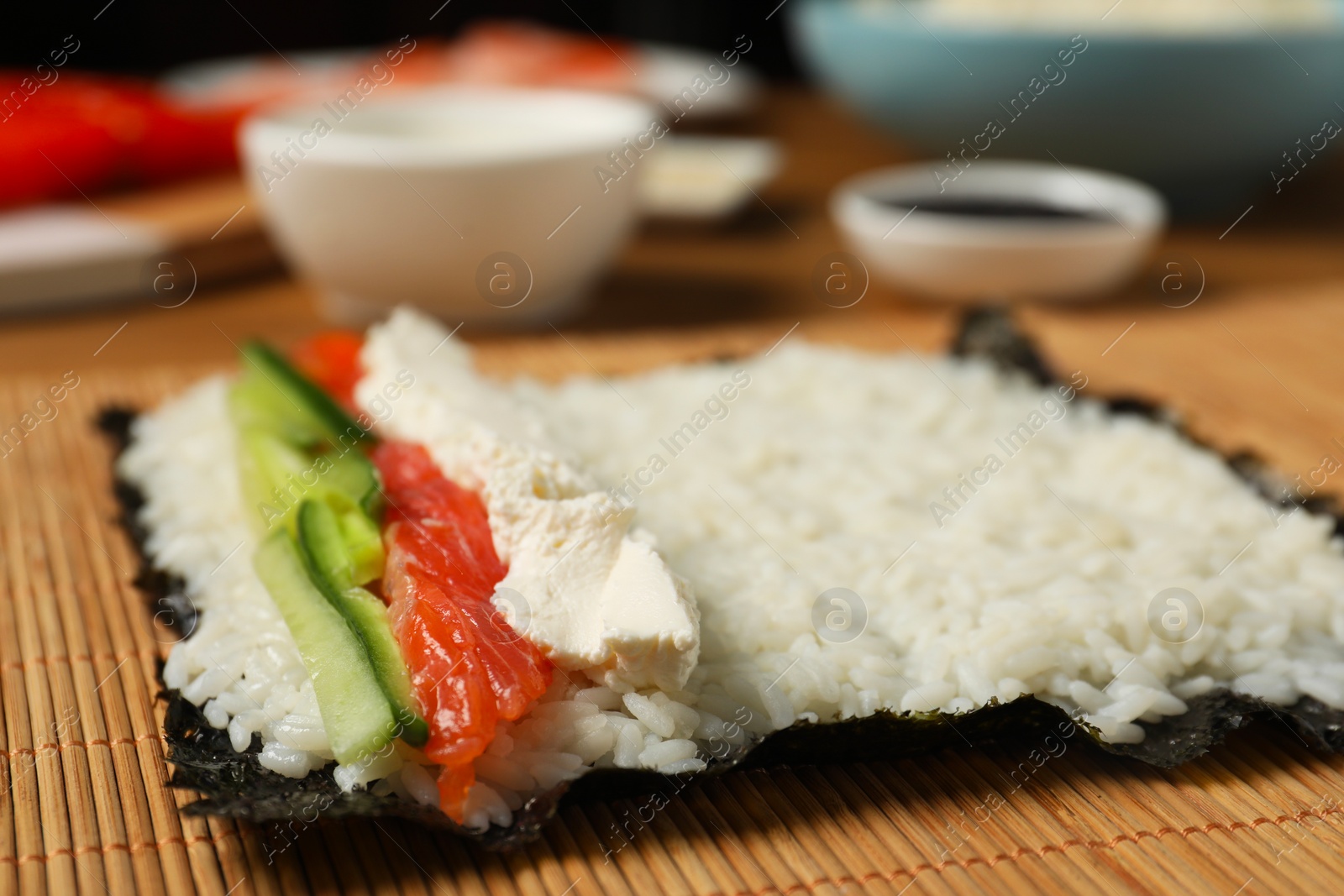 Photo of Unwrapped sushi roll with rice, cucumber, cheese and salmon on bamboo mat, closeup