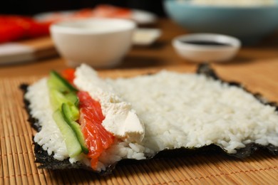 Photo of Unwrapped sushi roll with rice, cucumber, cheese and salmon on bamboo mat, closeup