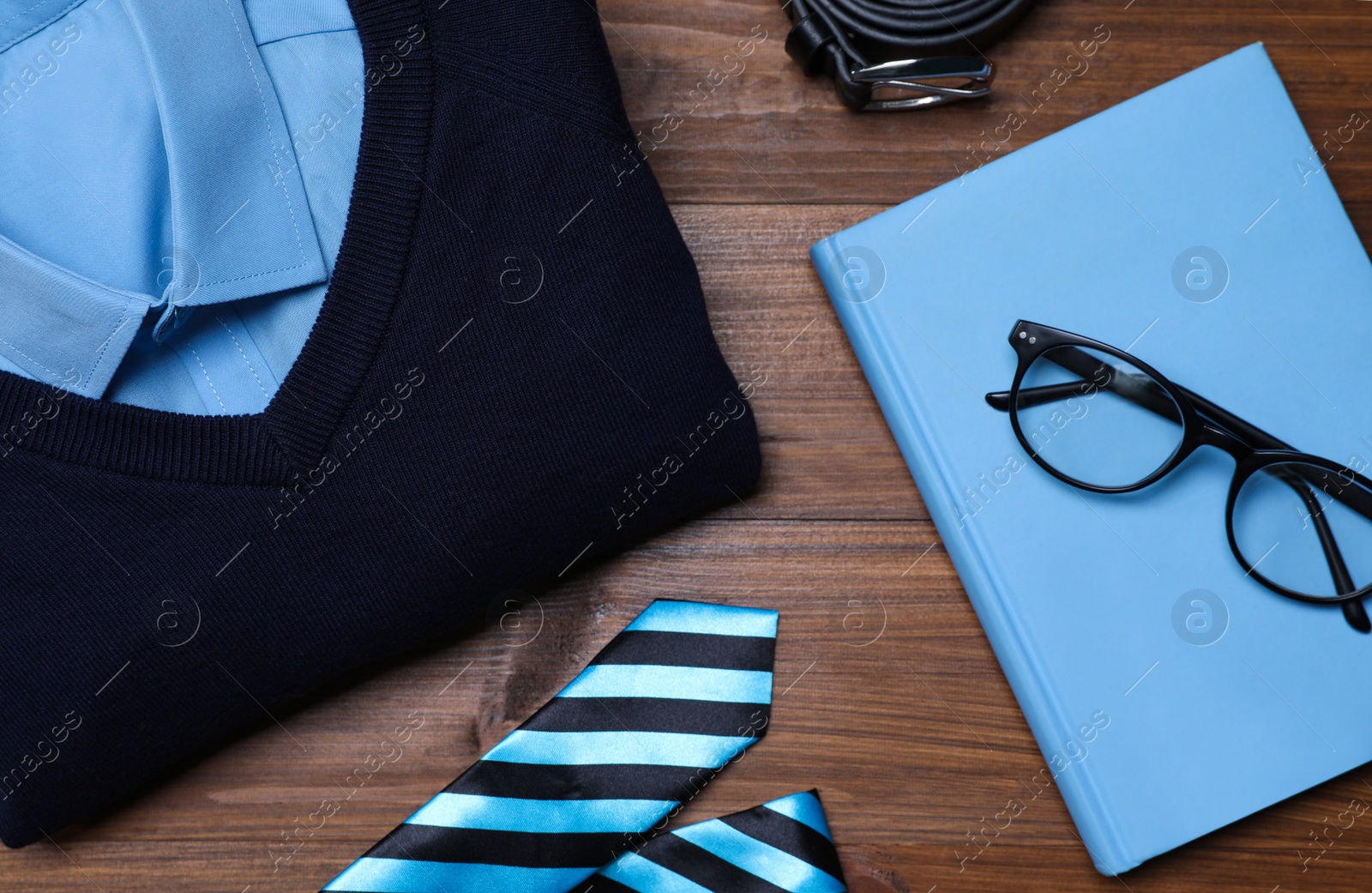 Photo of Stylish school uniform for boy, glasses and notebook on wooden background, flat lay