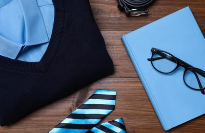 Stylish school uniform for boy, glasses and notebook on wooden background, flat lay