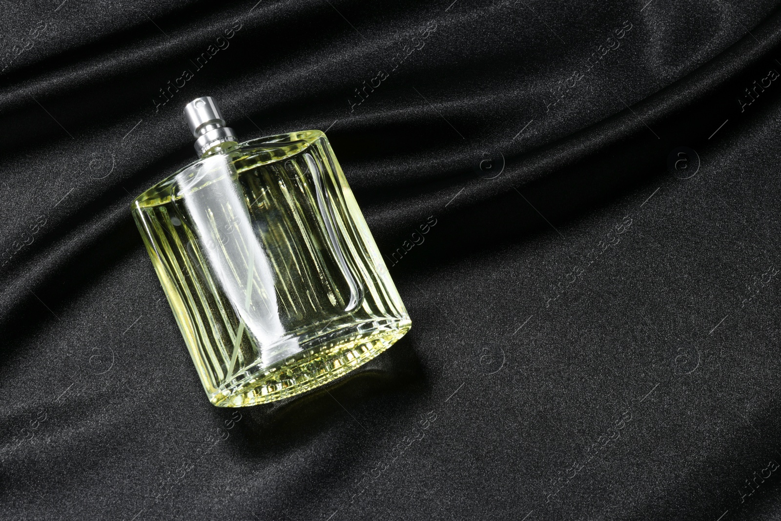 Photo of Luxury men's perfume in bottle on black satin fabric, space for text