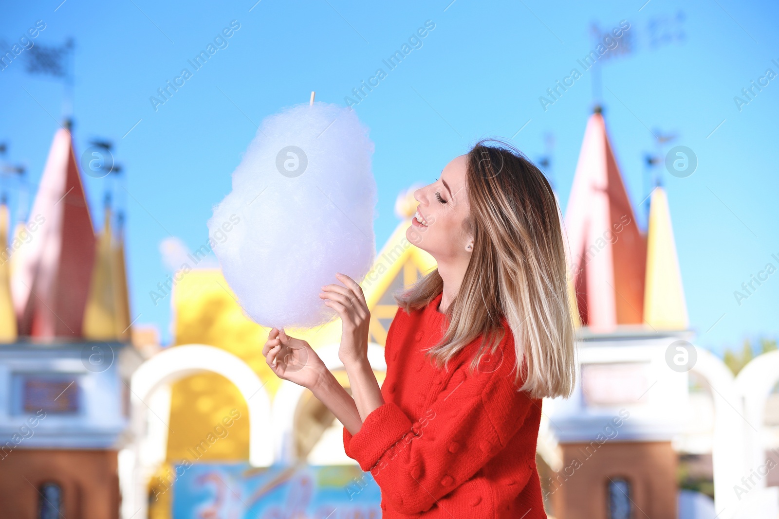 Photo of Young cheerful woman having fun with  cotton candy in amusement park