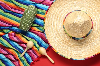 Mexican sombrero hat, toy cactus, maracas and colorful poncho on red background, flat lay