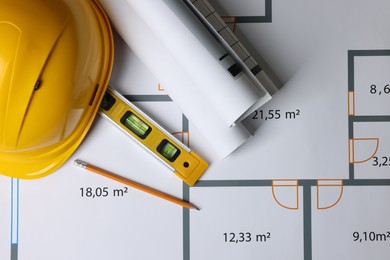 Photo of Rolled construction drawings, safety hat, pencil and bubble level on house plan, top view. Architect workspace