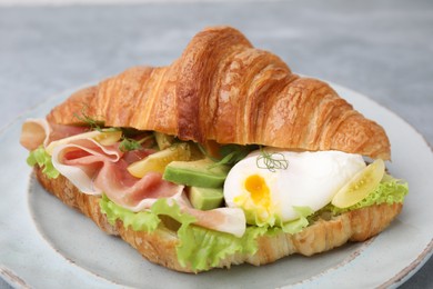 Photo of Delicious croissant with prosciutto, avocado and egg on grey table, closeup