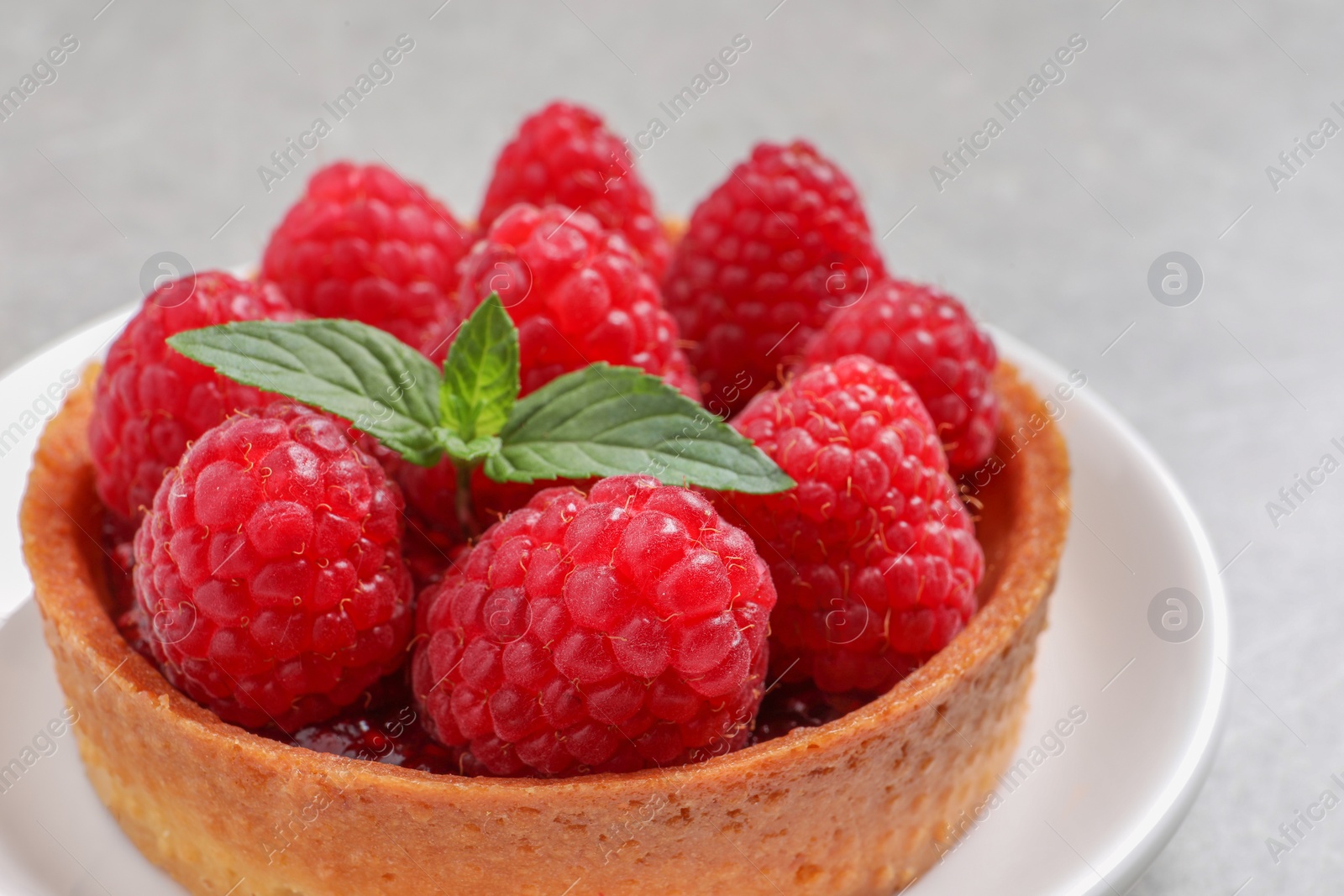 Photo of Tartlet with fresh raspberries and mint on light table, closeup. Delicious dessert