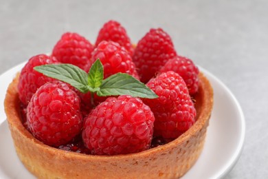 Photo of Tartlet with fresh raspberries and mint on light table, closeup. Delicious dessert