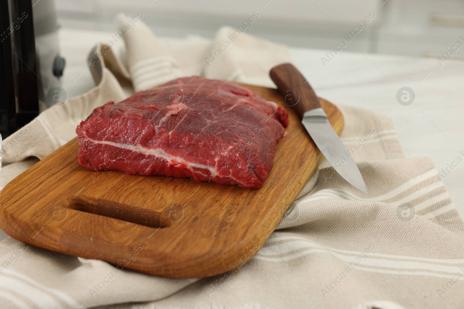 Photo of Board with beef meat and knife on white table indoors