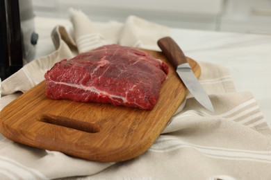 Photo of Board with beef meat and knife on white table indoors