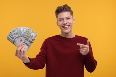 Photo of Happy man pointing at dollar banknotes on yellow background