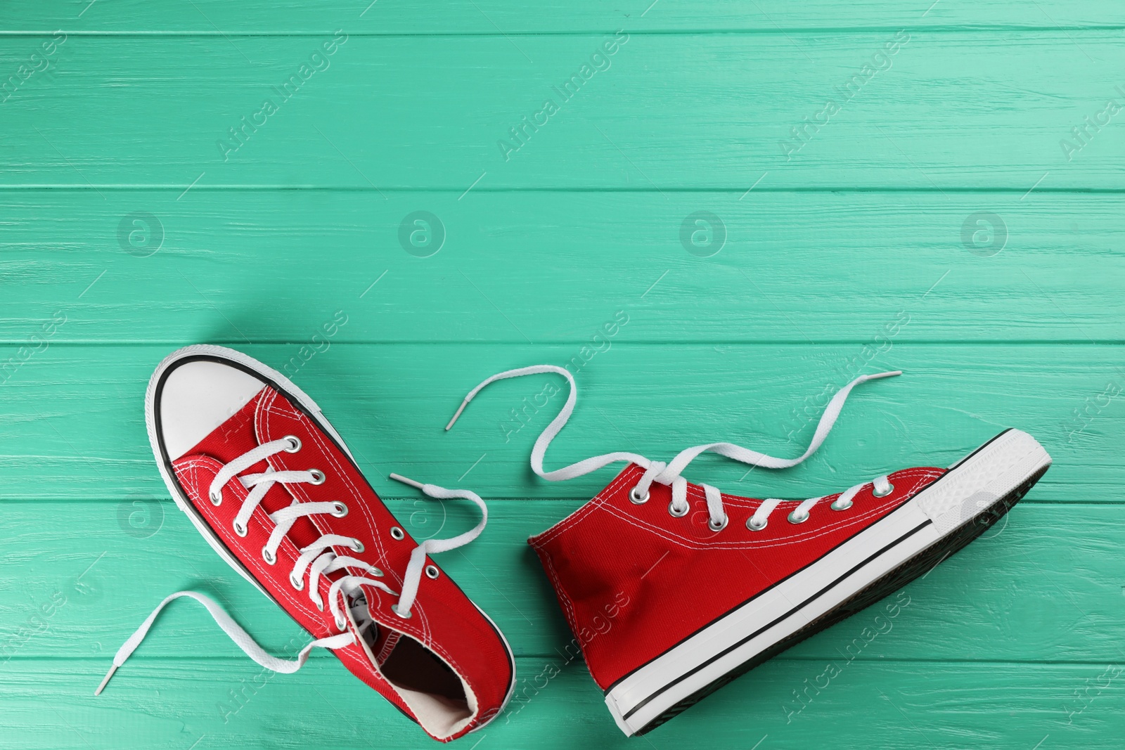 Photo of Pair of red sneakers on turquoise wooden table, flat lay. Space for text