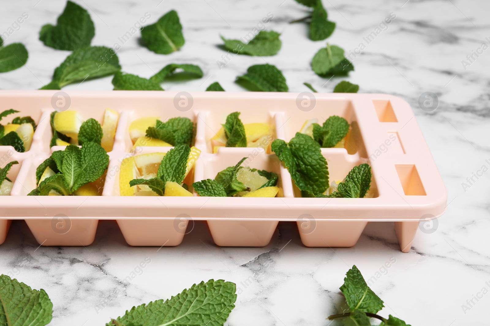 Photo of Ice cube tray with mint and lemon on marble table