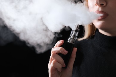 Photo of Young woman using electronic cigarette on black background, closeup