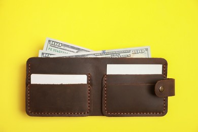 Photo of Stylish brown leather wallet with dollar banknotes on yellow background, top view