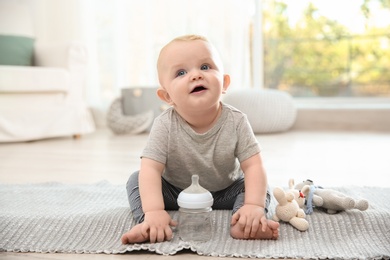 Cute baby with bottle sitting on floor in room