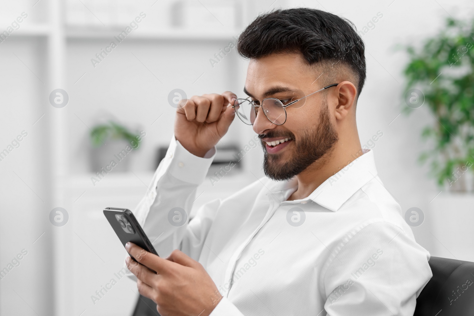 Photo of Happy young man using smartphone in office