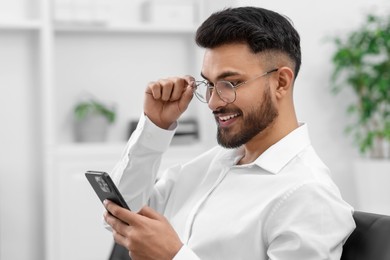 Photo of Happy young man using smartphone in office