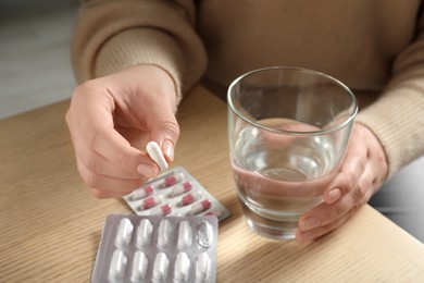 Woman with glass of water and pill at wooden table, closeup