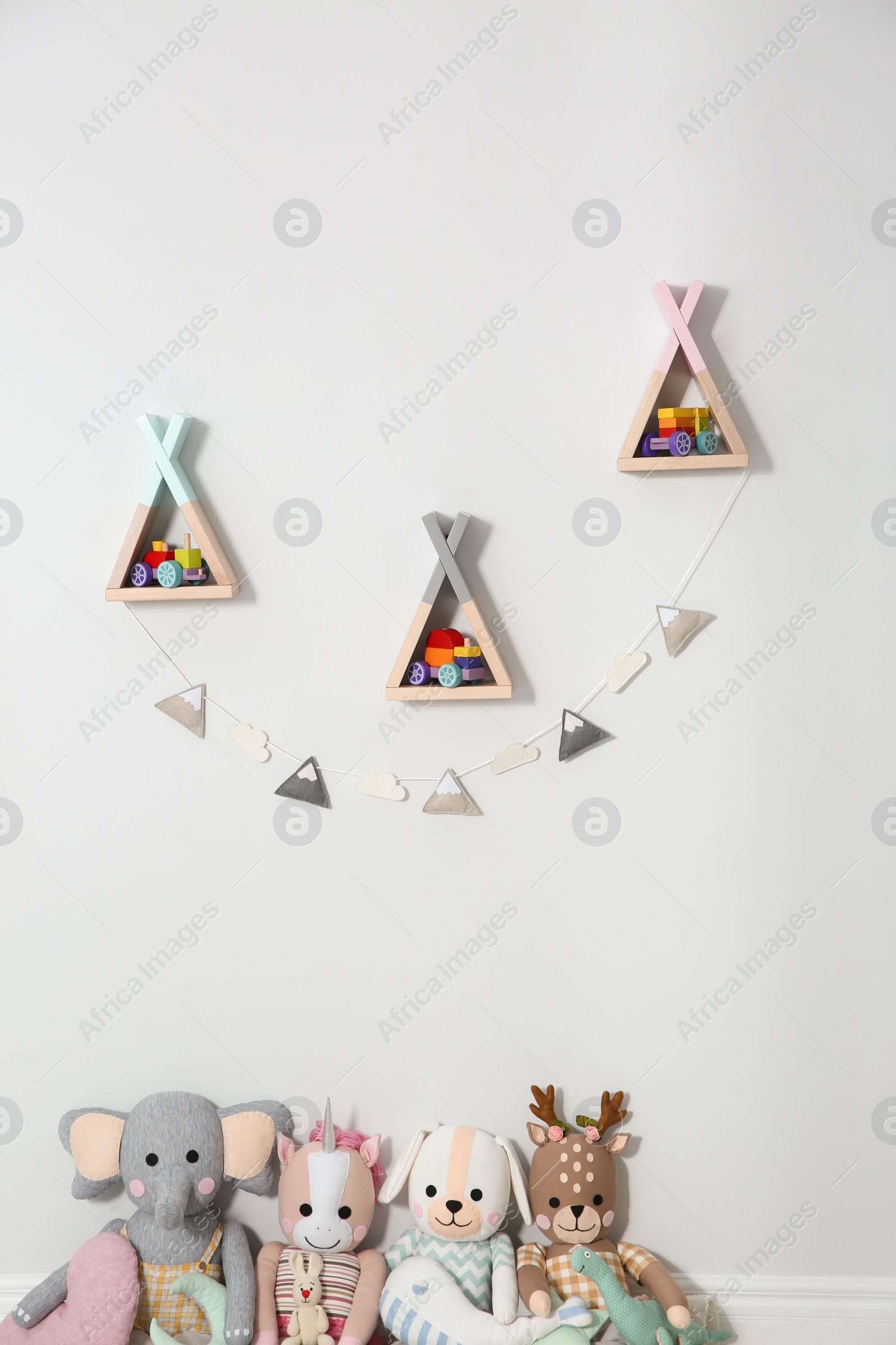 Photo of Wigwam shaped shelves, stuffed toys and garland indoors. Children's room interior design