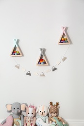 Photo of Wigwam shaped shelves, stuffed toys and garland indoors. Children's room interior design