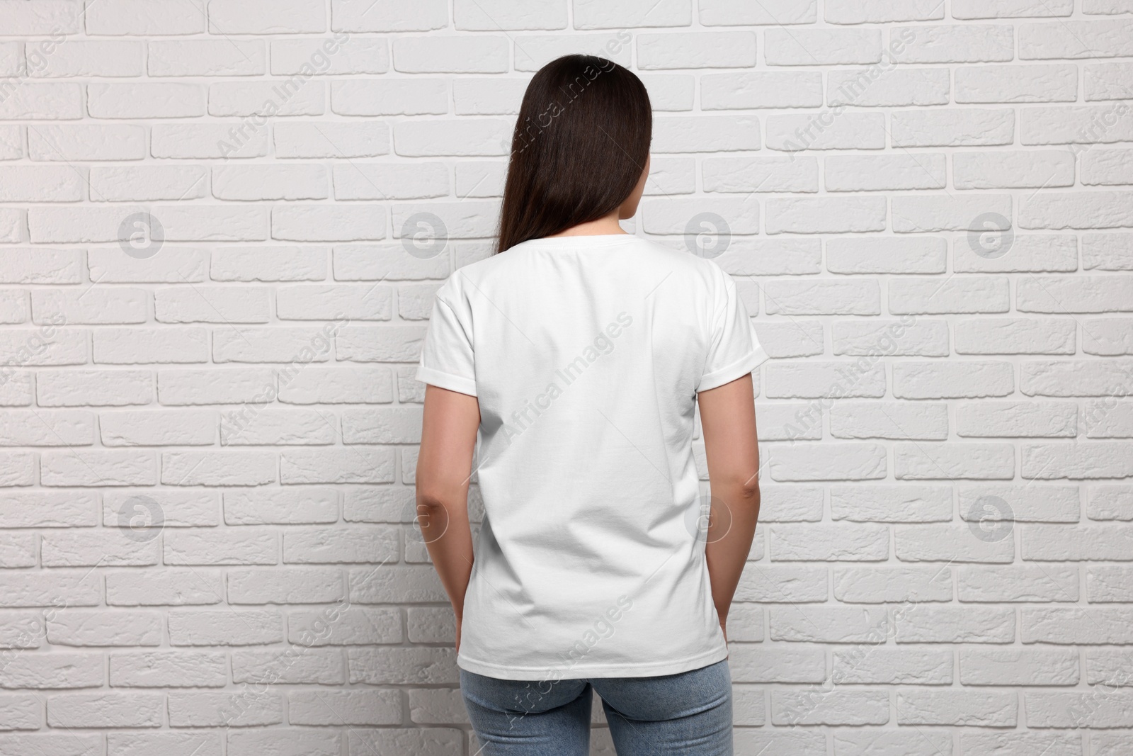 Photo of Woman wearing stylish T-shirt near white brick wall, back view