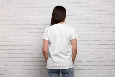 Woman wearing stylish T-shirt near white brick wall, back view