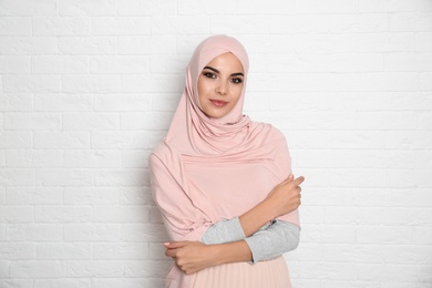 Portrait of young Muslim woman in hijab against brick wall