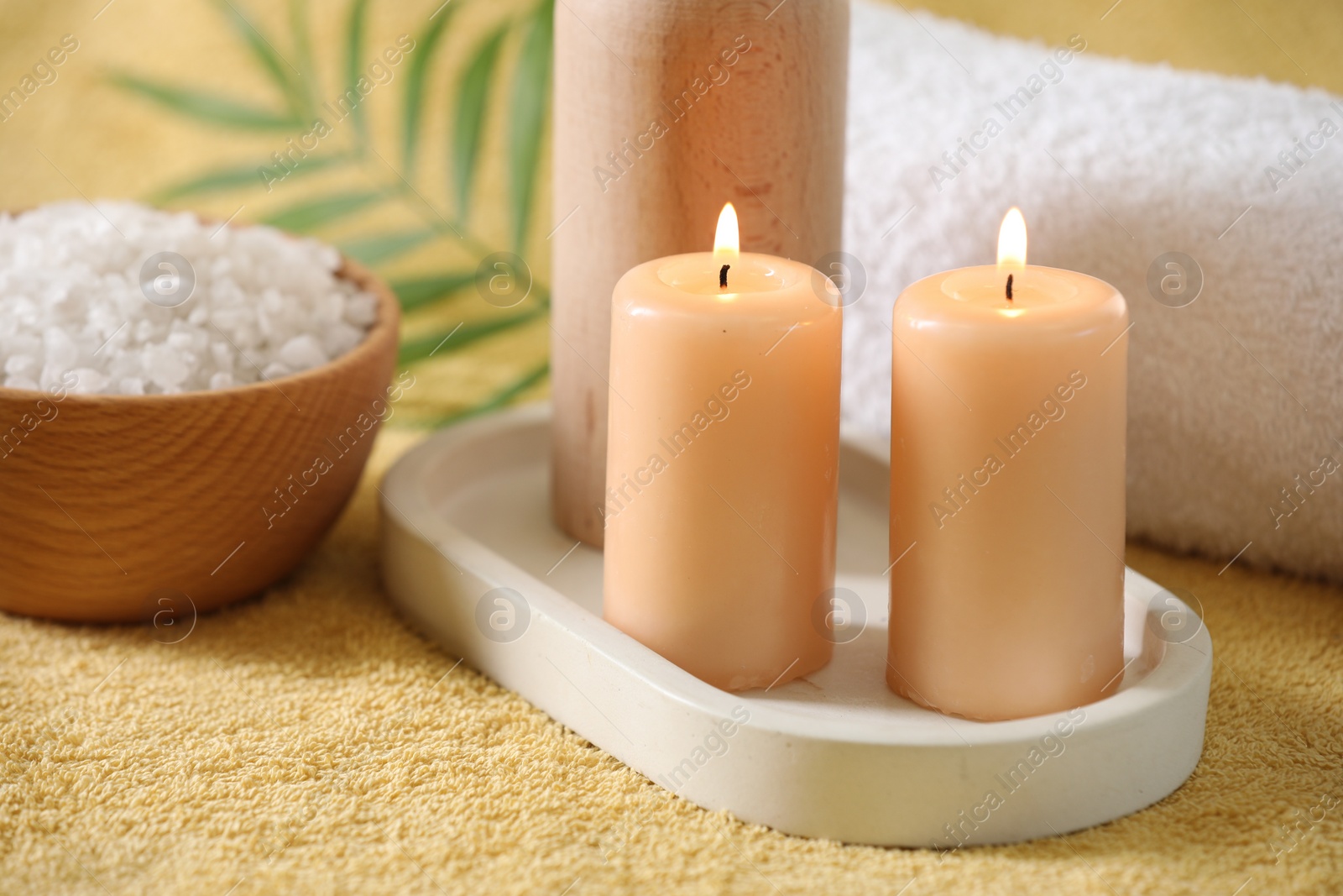 Photo of Spa composition. Burning candles, sea salt and towel on soft yellow fabric