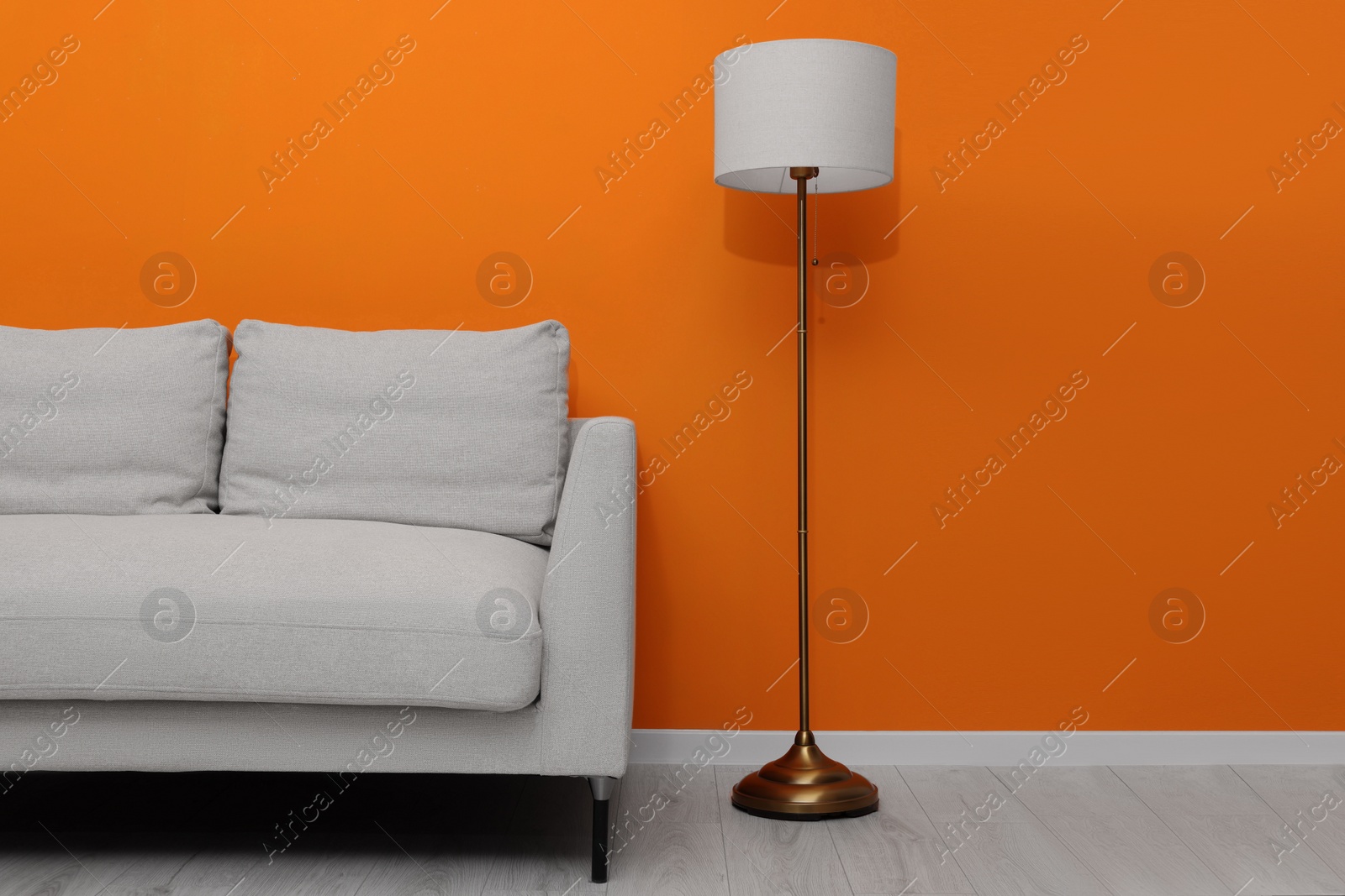 Photo of Comfortable sofa and stylish lamp near orange wall indoors