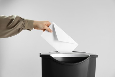 Photo of Woman destroying envelope with shredder on grey background, closeup