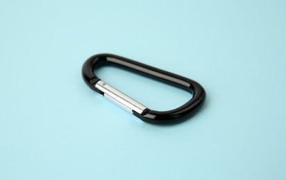 Photo of One black carabiner on light blue background, closeup