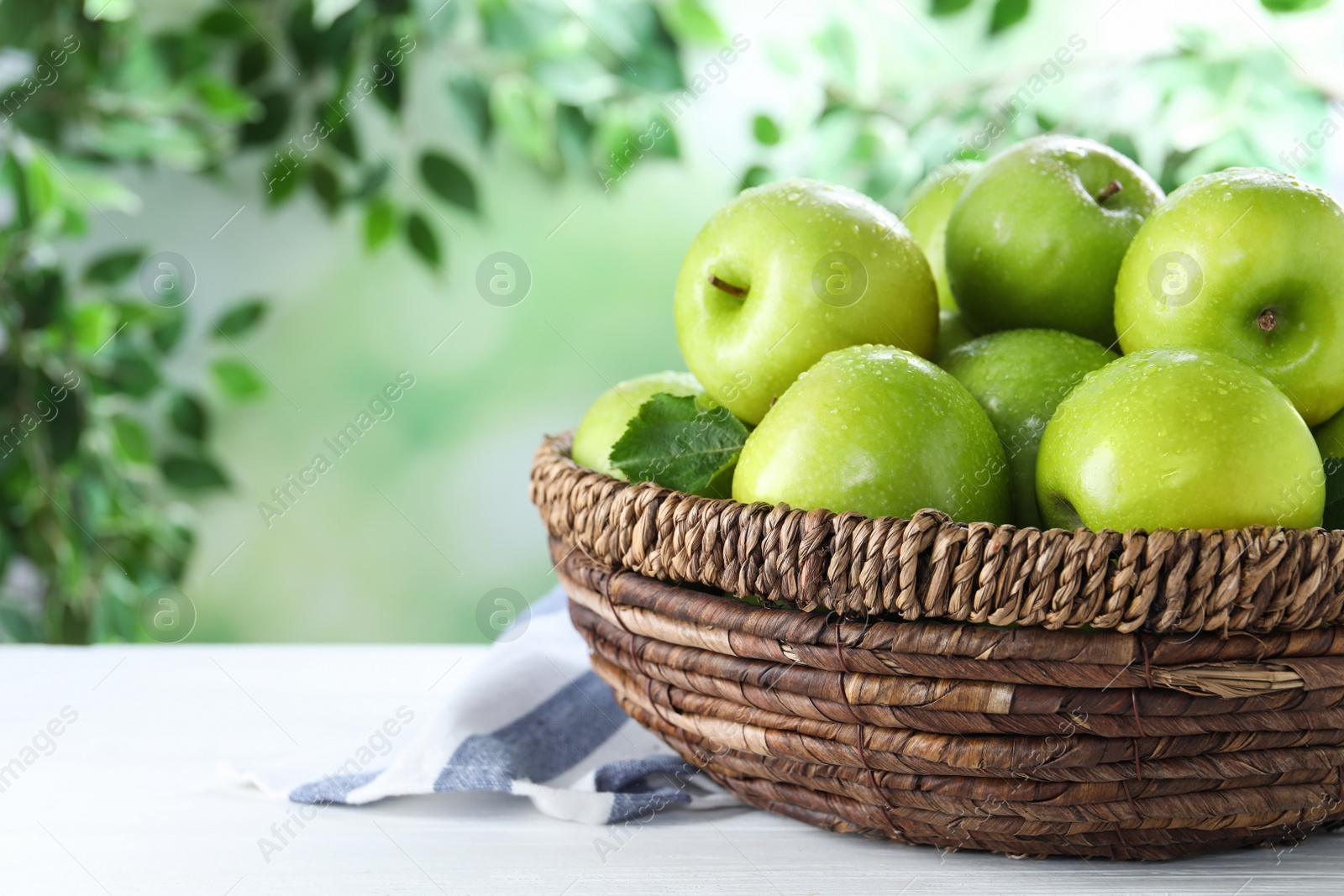 Photo of Juicy green apples in wicker basket on white wooden table outdoors