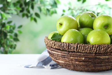 Juicy green apples in wicker basket on white wooden table outdoors