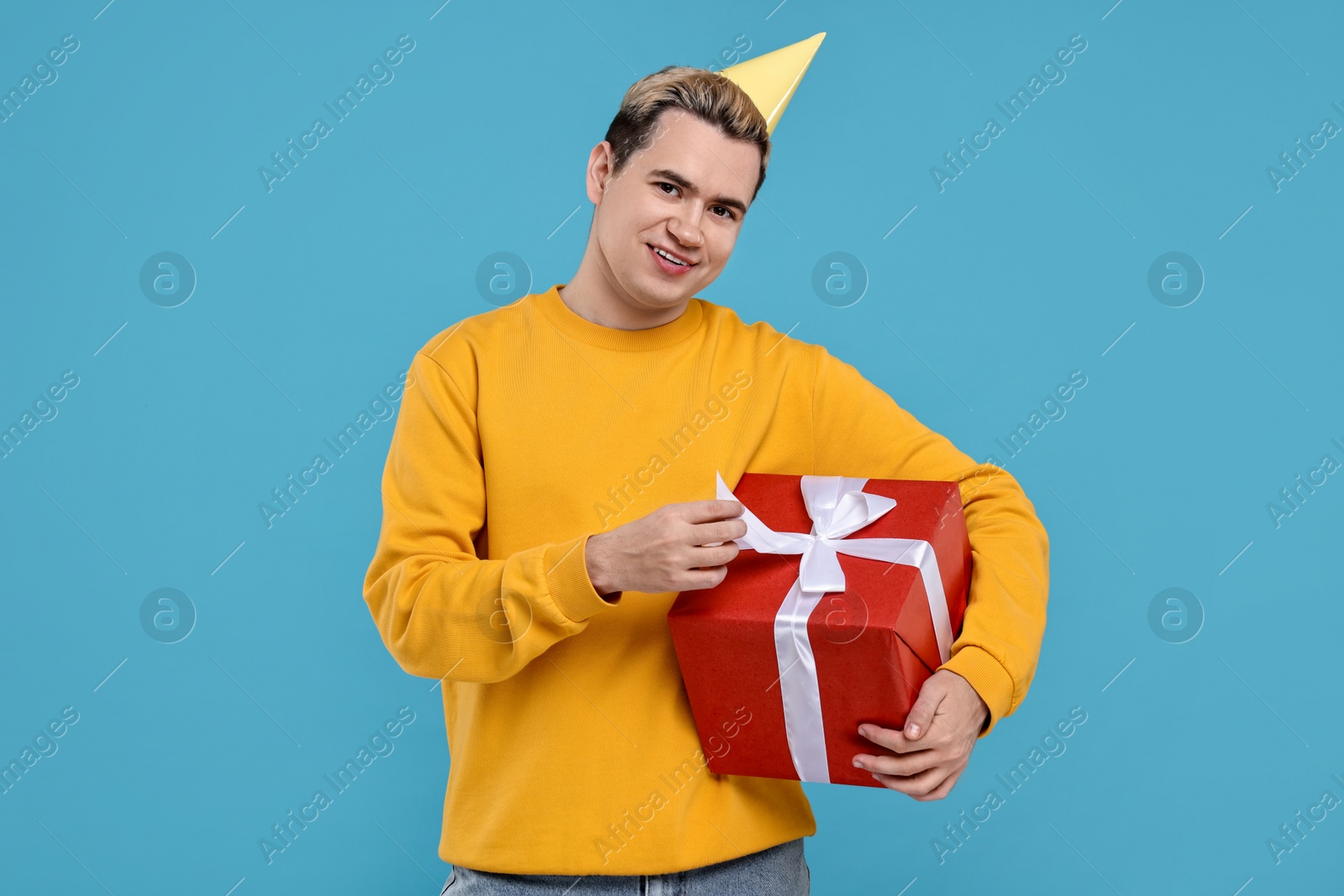 Photo of Young man with party hat and gift box on light blue background