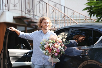 Young handsome man with beautiful flower bouquet near car on street