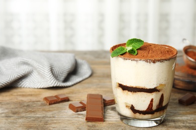 Glass of tiramisu cake and chocolate on wooden table, space for text