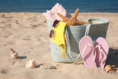 Bag with beach accessories and flip flops on sand near sea