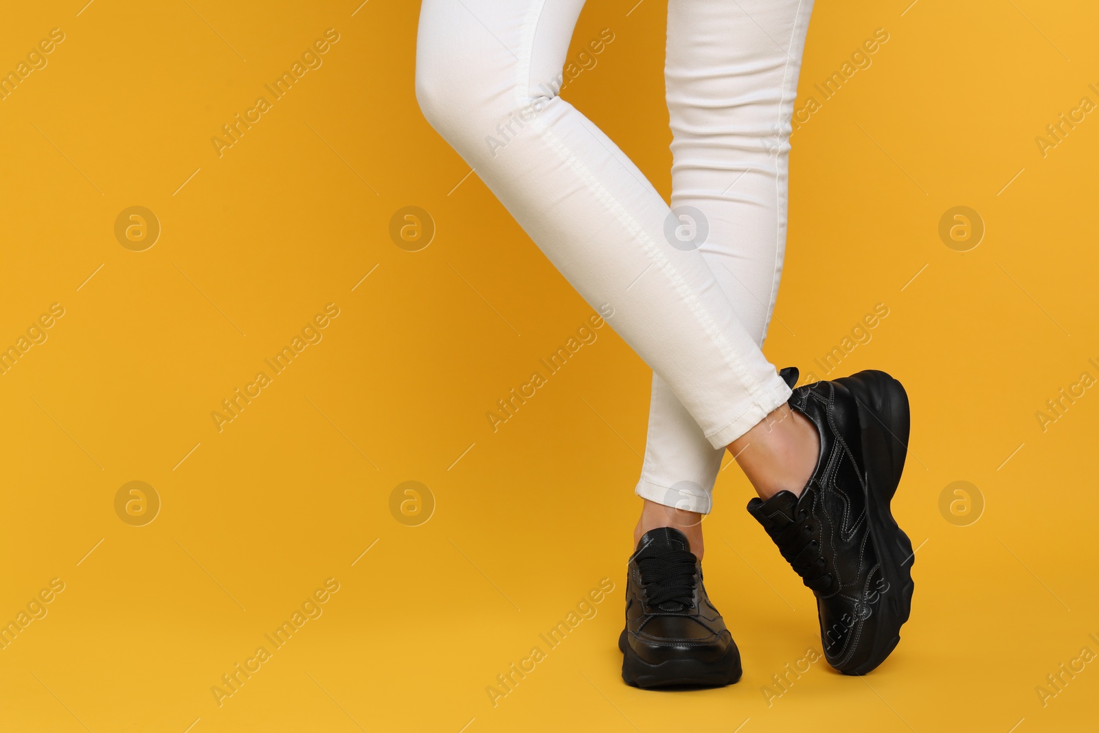 Photo of Woman wearing stylish sneakers on yellow background, closeup. Space for text