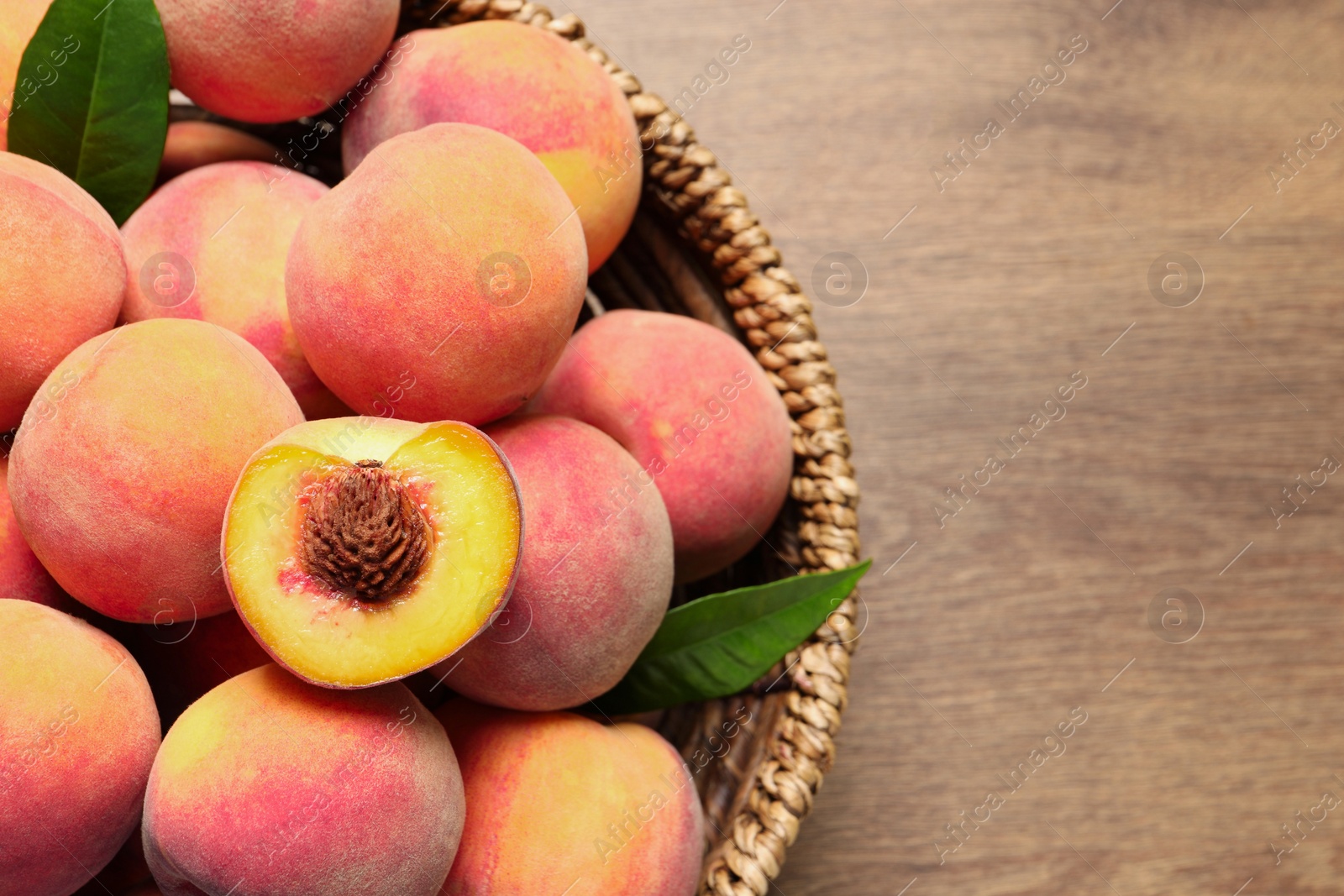 Photo of Cut and whole fresh ripe peaches with green leaves in basket on wooden table, top view. Space for text