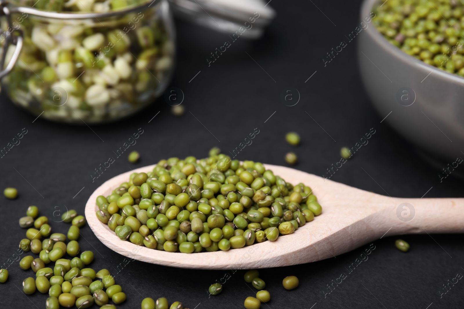 Photo of Different dishware with green mung beans on black background, closeup