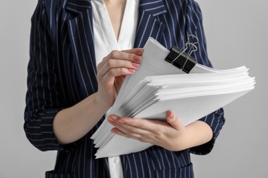 Photo of Woman attaching documents with metal binder clip on grey background, closeup