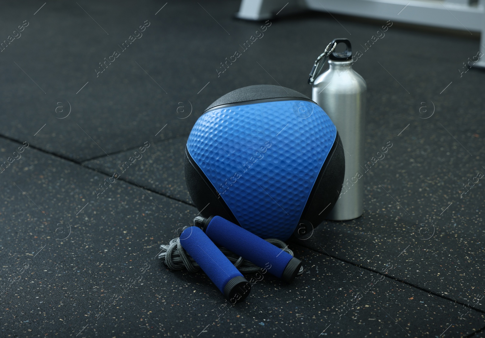 Photo of Blue medicine ball, bottle and skipping rope on floor in gym, space for text