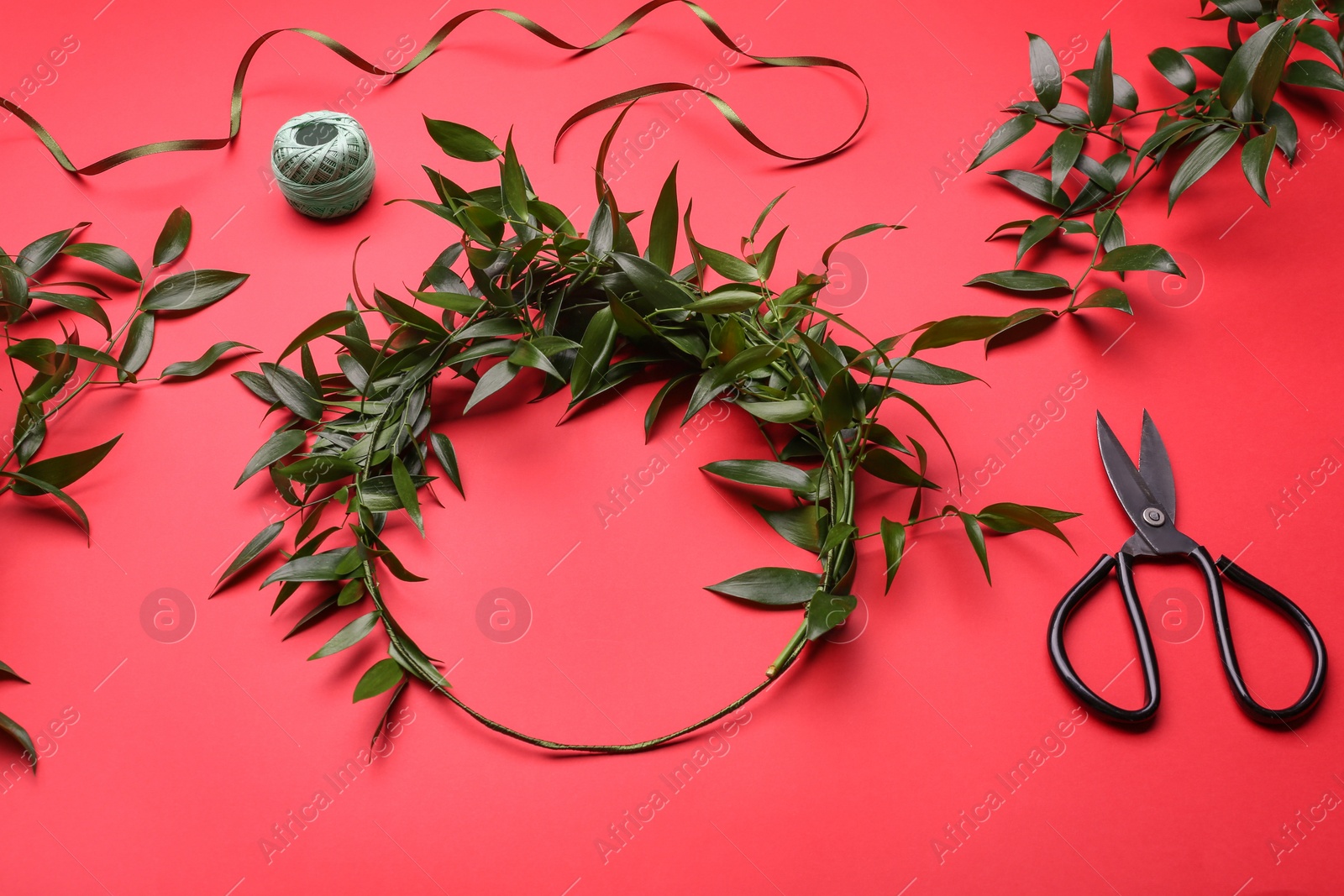 Photo of Unfinished mistletoe wreath and florist supplies on red background. Traditional Christmas decor