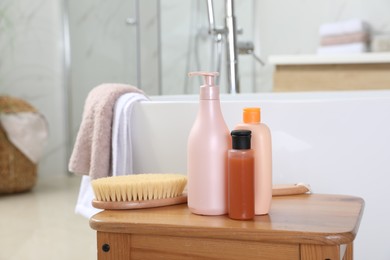 Photo of Bottles of shower gels and brush on wooden table near tub in bathroom, space for text