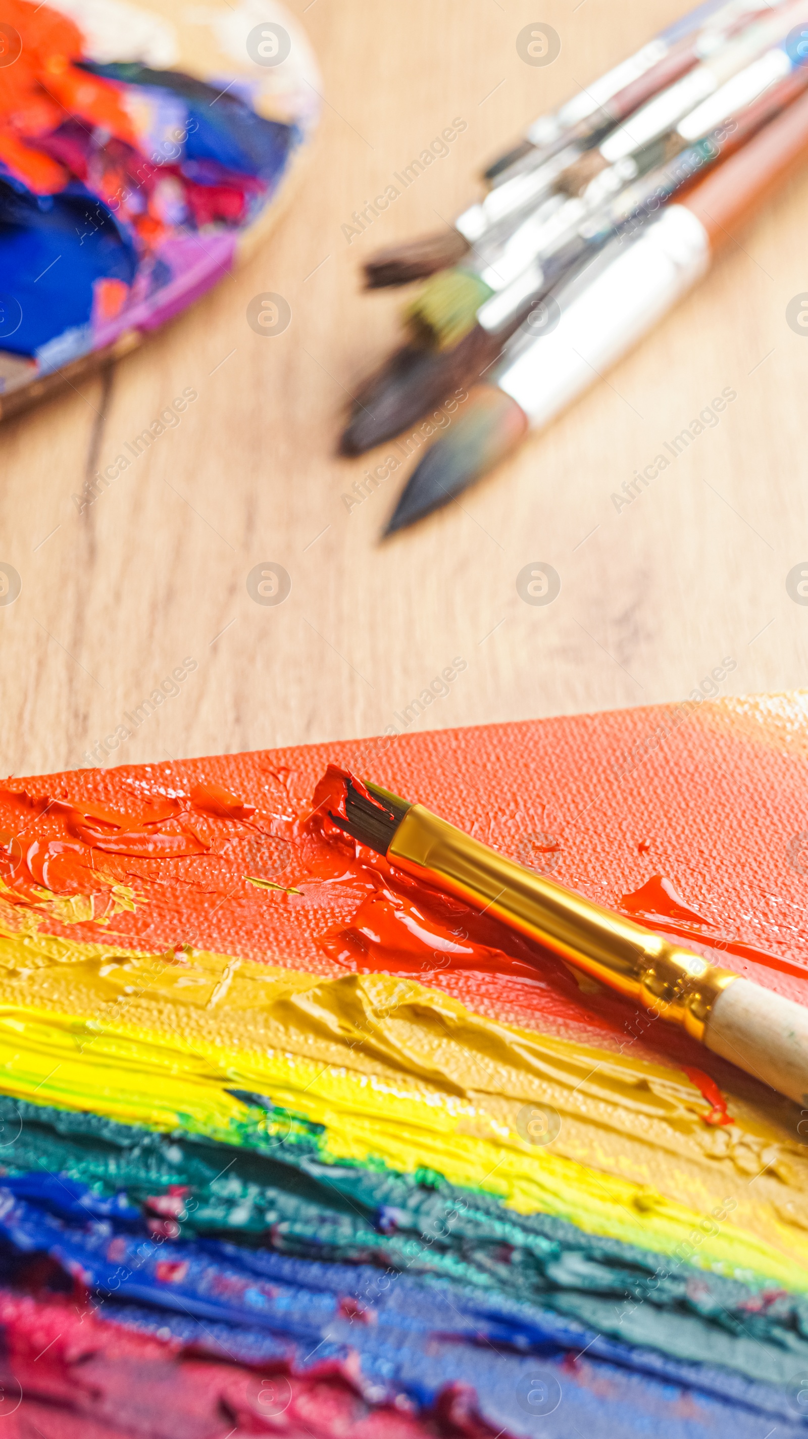 Photo of Brushes and artist's palettes with colorful mixed paints on wooden table, closeup